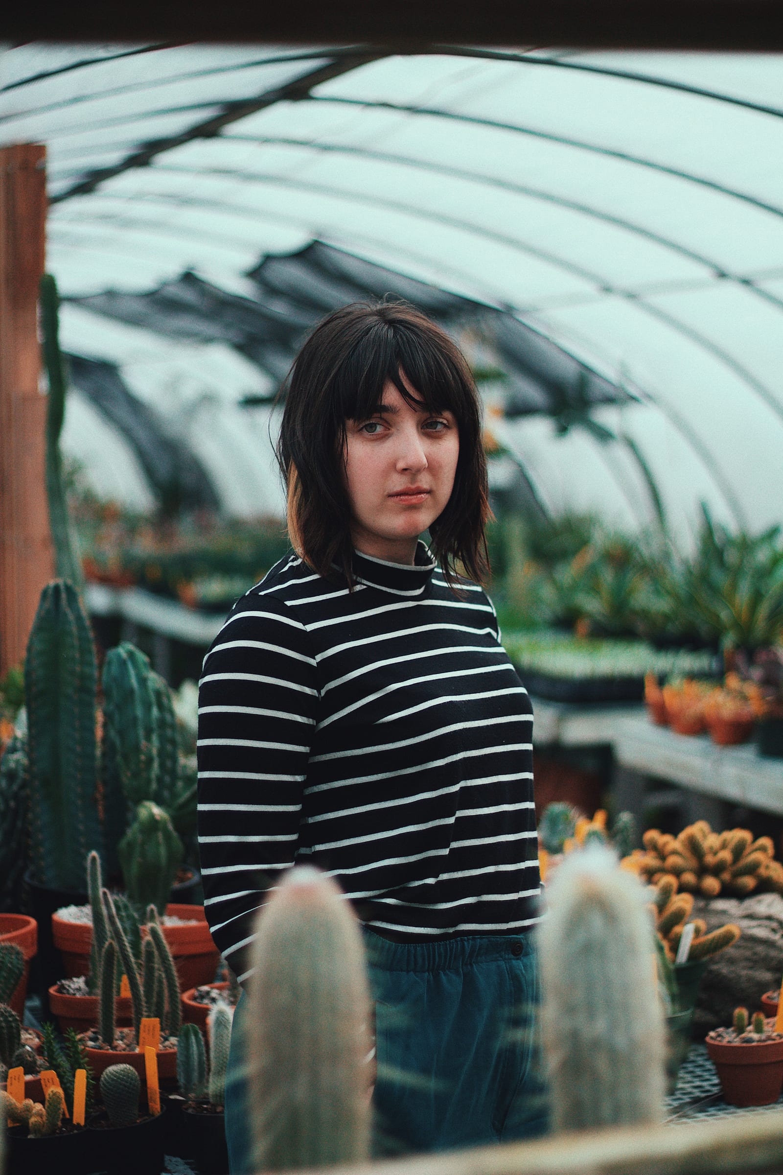 A woman standing among plants inside a lush greenhouse examining the growth of green plants