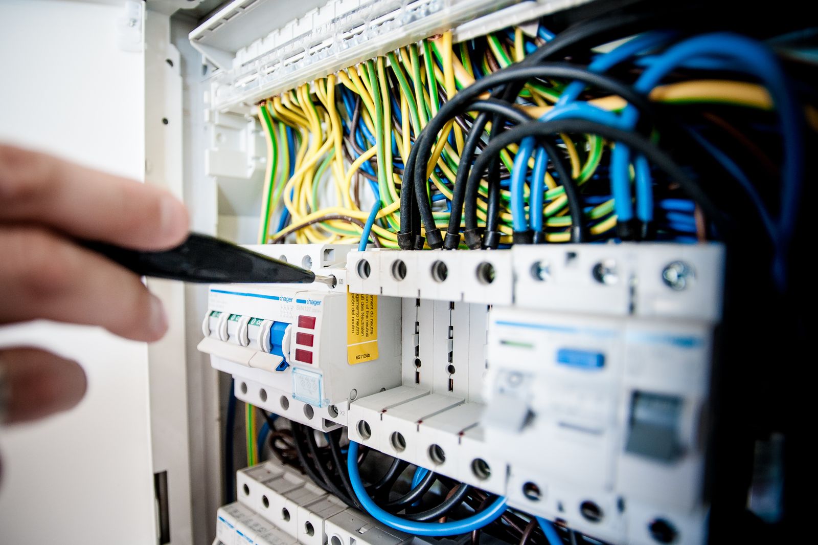 An electrician's hand working on a circuit breaker panel with multiple colorful wires connected to breakers