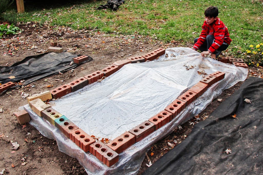 A homemade wooden cold frame being planted, set on a leveled garden bed