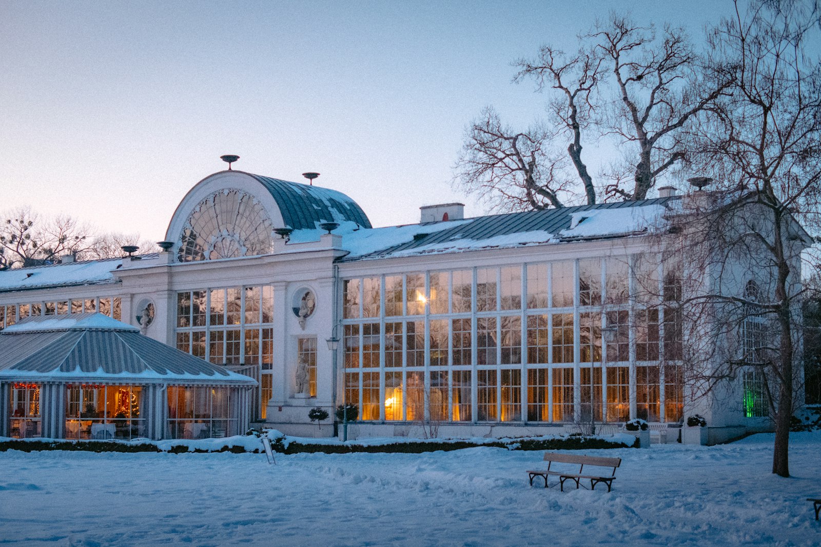 An orangery building with glass-and-masonry construction surrounded by snow-covered grounds in winter