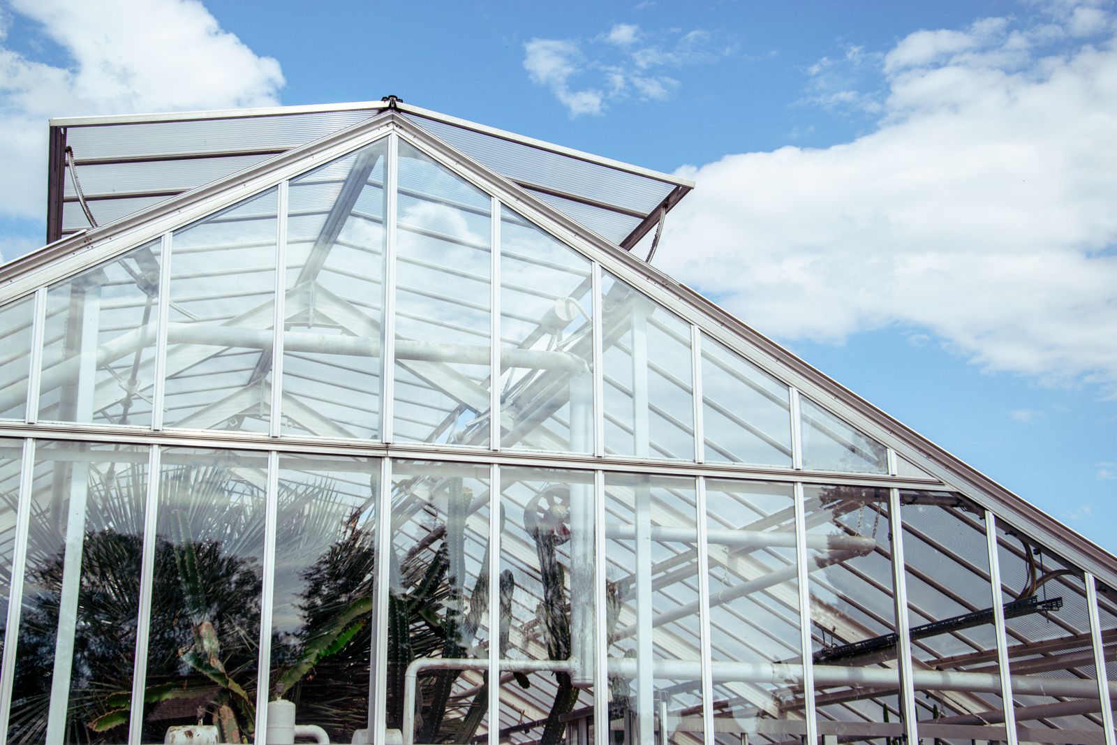 A modern glass greenhouse structure with geometric glazing panels against a clear blue sky