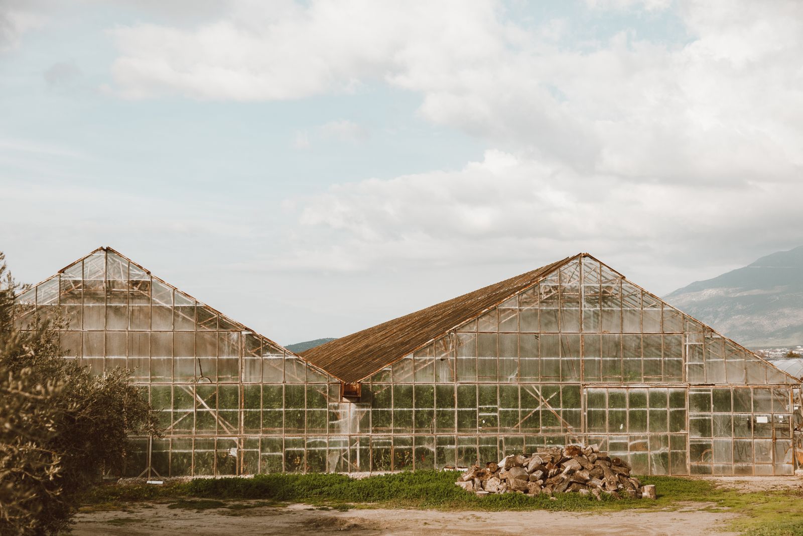 Two low-profile greenhouse structures in a rural setting under an overcast sky